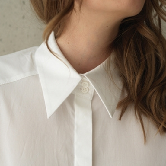 White button up shirt with a curved hem and wide collar, with three buttons  at the neck. 