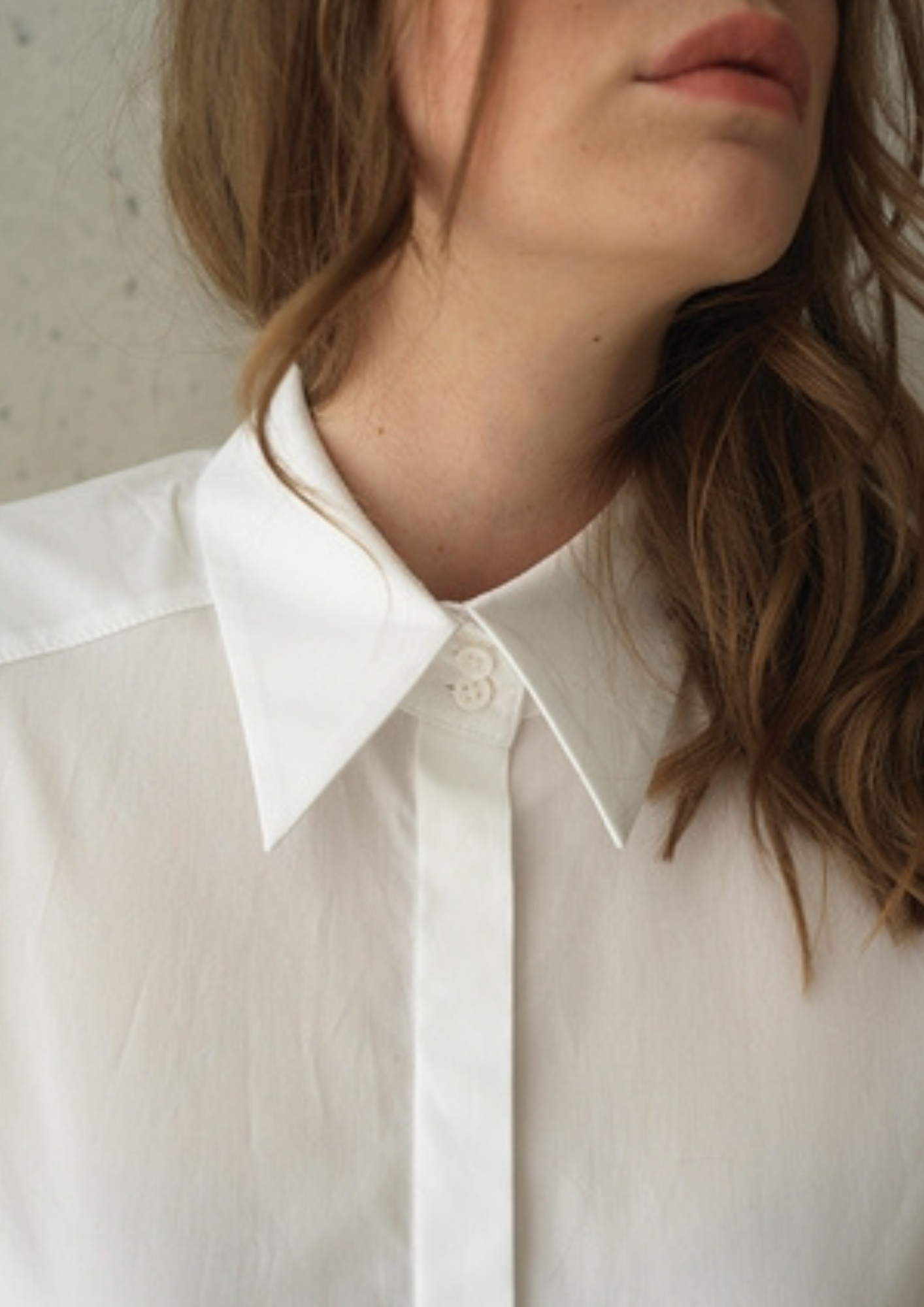 White button up shirt with a curved hem and wide collar, with three buttons  at the neck. 