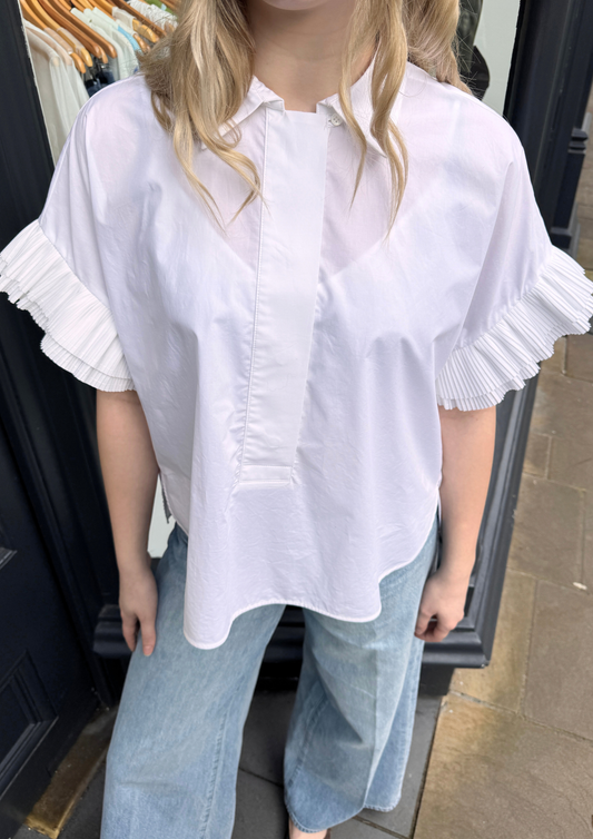 Person wearing a white blouse with ruffled sleeves and light blue jeans.