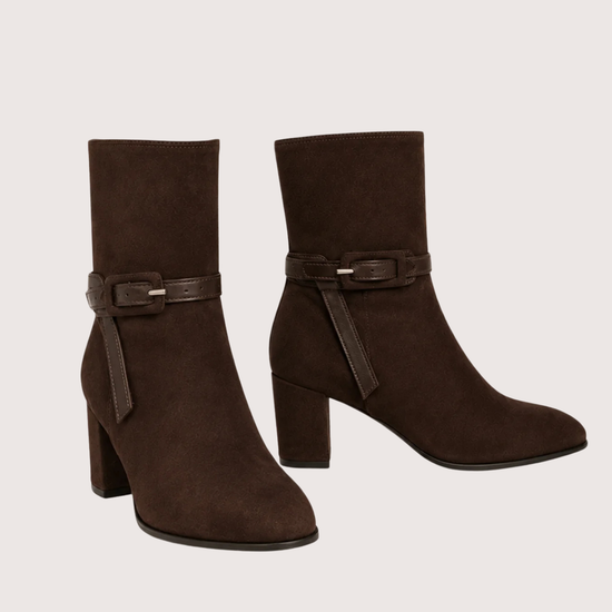 A pair of dark brown suede ankle boots with block heels and a matching faux-leather buckle strap around the ankle, shown against a plain light beige background.