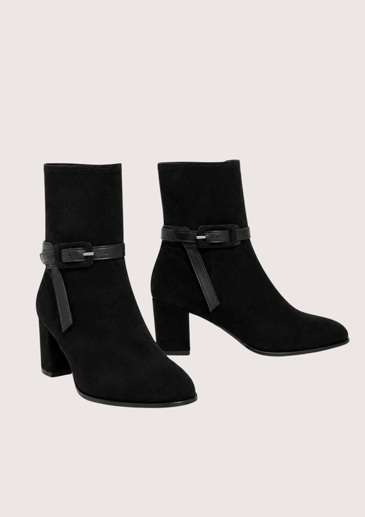 A pair of black suede ankle boots with block heels and a decorative strap detail across the ankle, shown against a light beige background.