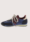 A low-top fashion sneaker, featuring navy blue suede and mesh panels, burgundy accents, patterned white and burgundy laces, and a cream midsole, shown against a plain light gray background.