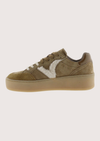 A low-top platform sneaker in taupe brown suede and leather, featuring a contrasting white faux-fur panel on the side and a thick tan sole.