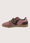 A low-top sneaker in dusty pink and dark burgundy suede with olive green laces and a gum sole, shown in profile against a light beige background.