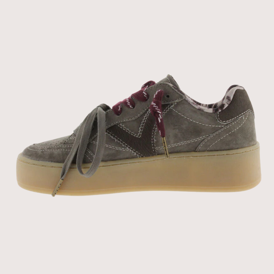 A low-top platform sneaker in dark gray suede and leather, featuring a thick beige gum sole, gray laces, and burgundy ribbon laces tied in a bow.
