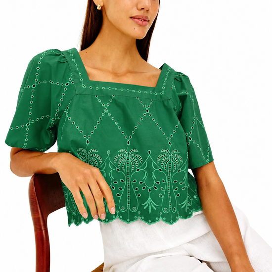 Woman wearing a green embroidered blouse sitting on a chair with a white background