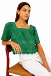 Woman wearing a green embroidered blouse sitting on a chair with a white background