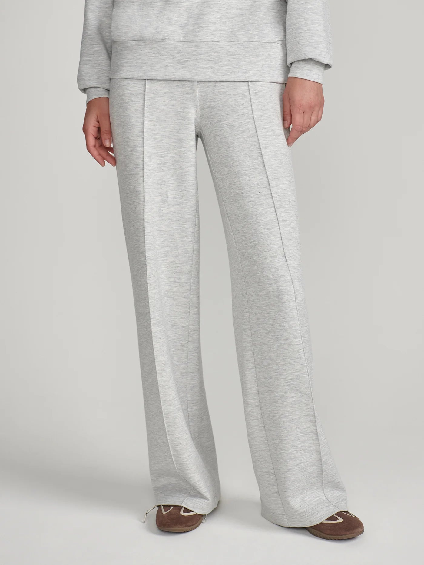 A person wearing light heather gray wide-leg sweatpants with a matching sweatshirt partially visible, standing against a plain light gray studio background.