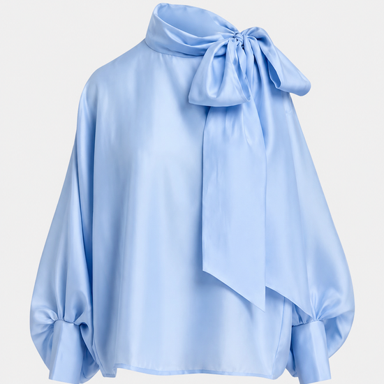 A light blue satin blouse with a large bow at the high neck and gathered balloon sleeves, shown on a plain light gray background.