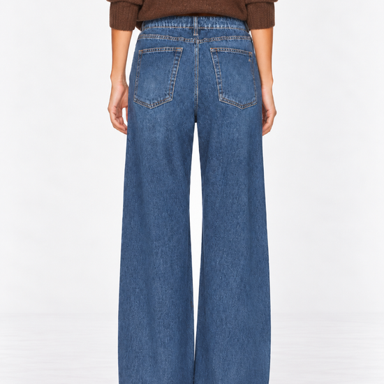 A person shown from the back wearing wide-leg blue denim jeans and a brown long-sleeve top against a plain white studio background.