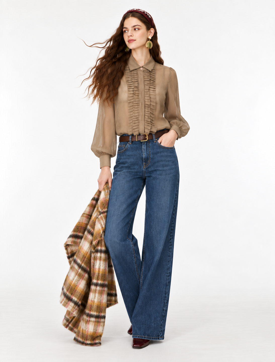 A woman modeling a beige long-sleeve blouse with vertical ruffles, paired with blue wide-leg jeans and holding a brown and beige plaid coat against a plain white studio background.