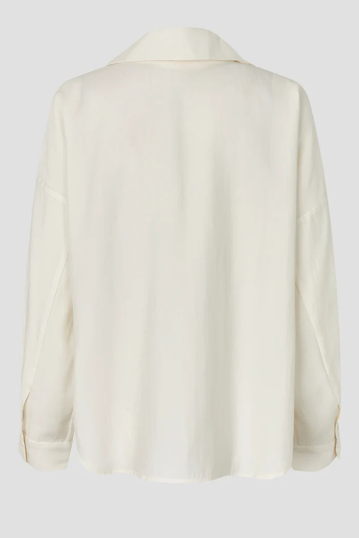 An off-white long-sleeve shirt shown from the back, featuring a relaxed fit and a subtle textured fabric, set against a solid light gray background.