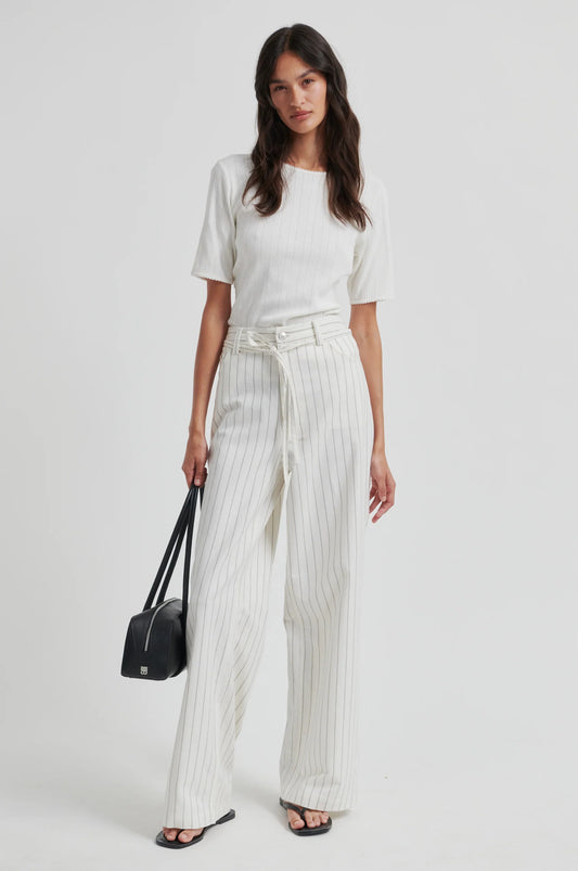 Woman wearing a white top and striped pants holding a black handbag on a white background from Second Female