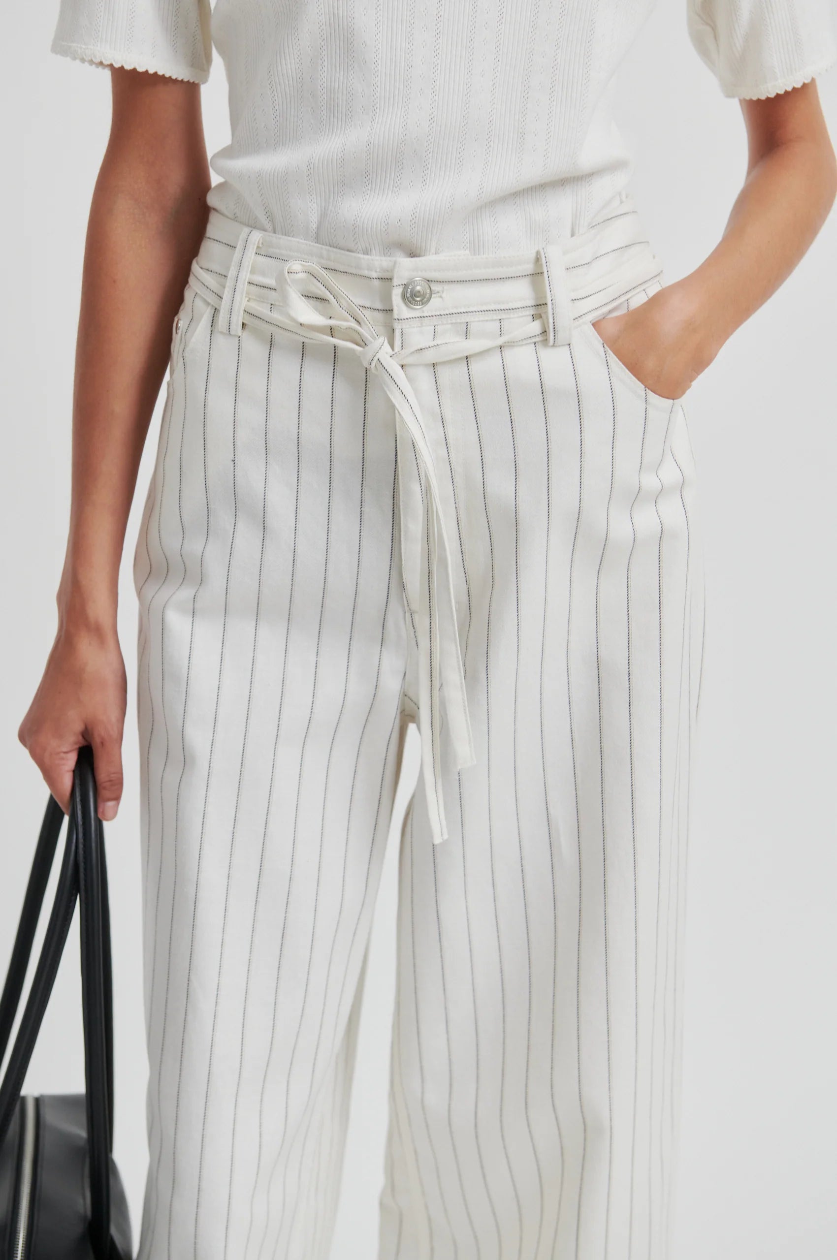Person wearing a white top and pinstripe pants with a black handbag.