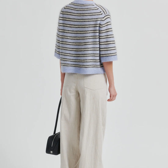 Rear view of Woman wearing a striped sweater and wide-leg pants with a black handbag on a light gray background