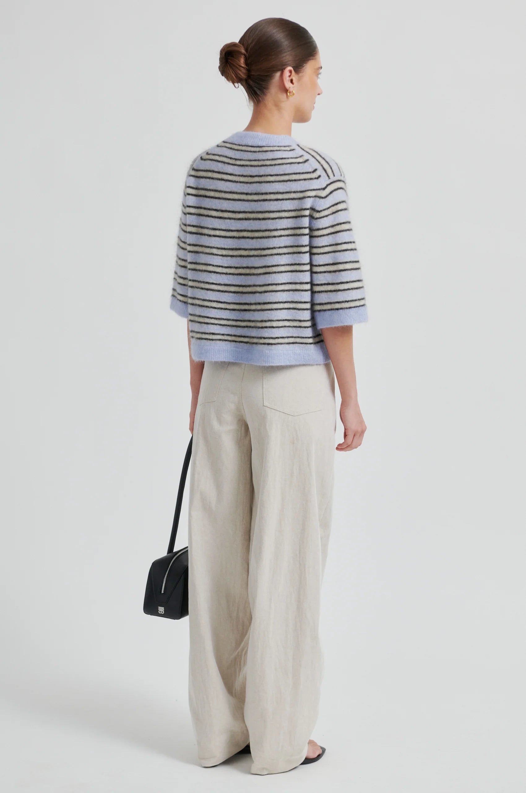 Rear view of Woman wearing a striped sweater and wide-leg pants with a black handbag on a light gray background