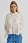 Woman wearing a sheer white blouse with long sleeves and blue jeans on a white background from second female