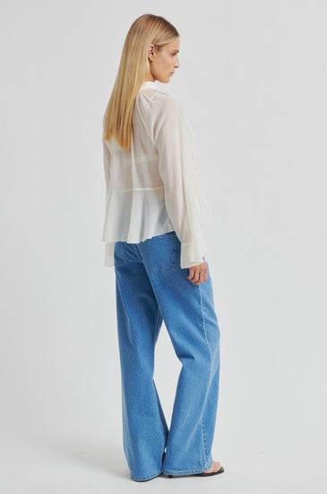 Woman wearing a light-colored blouse and blue jeans on a white background rear view from second female