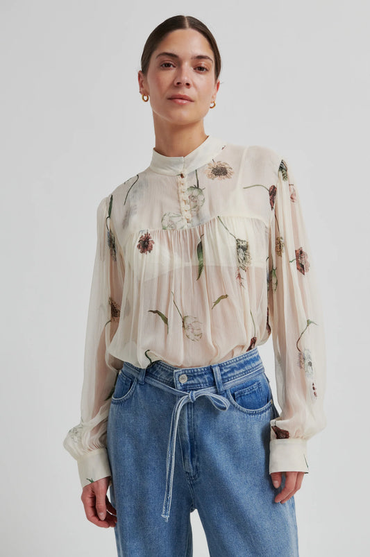 Woman wearing a semi sheer floral blouse and blue jeans on a white background from Second Female