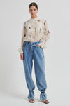 Woman wearing a floral blouse and blue jeans on a white background from Second Female