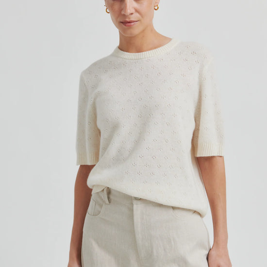 Woman wearing a cream-colored sweater and pants against a white background from second female