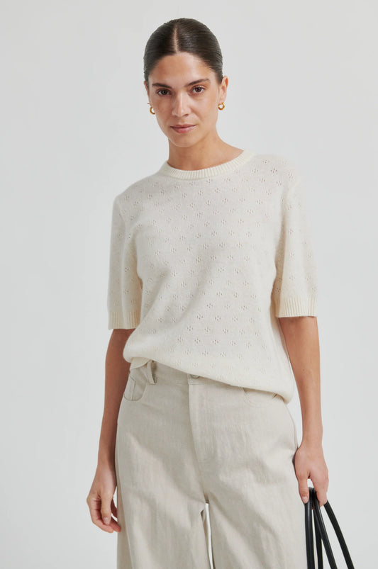 Woman wearing a cream-colored sweater and pants against a white background from second female