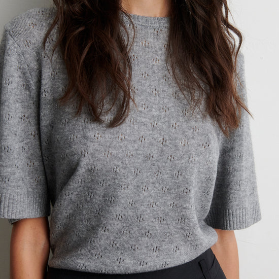 Person wearing a gray patterned top with black pants on a white background from second female