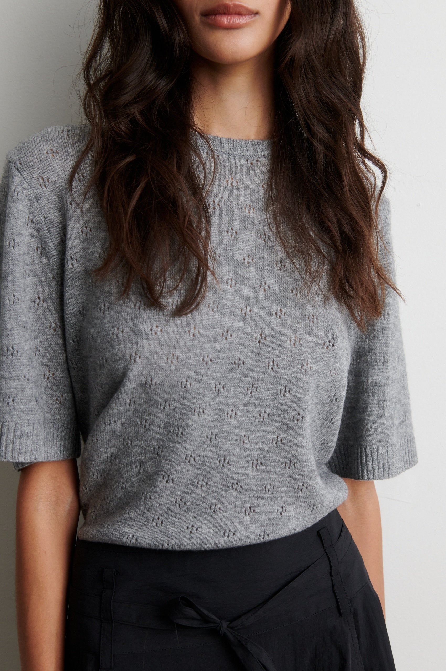 Person wearing a gray patterned top with black pants on a white background from second female
