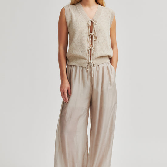 Woman wearing a beige sleeveless top and wide-leg pants on a white background from second Female