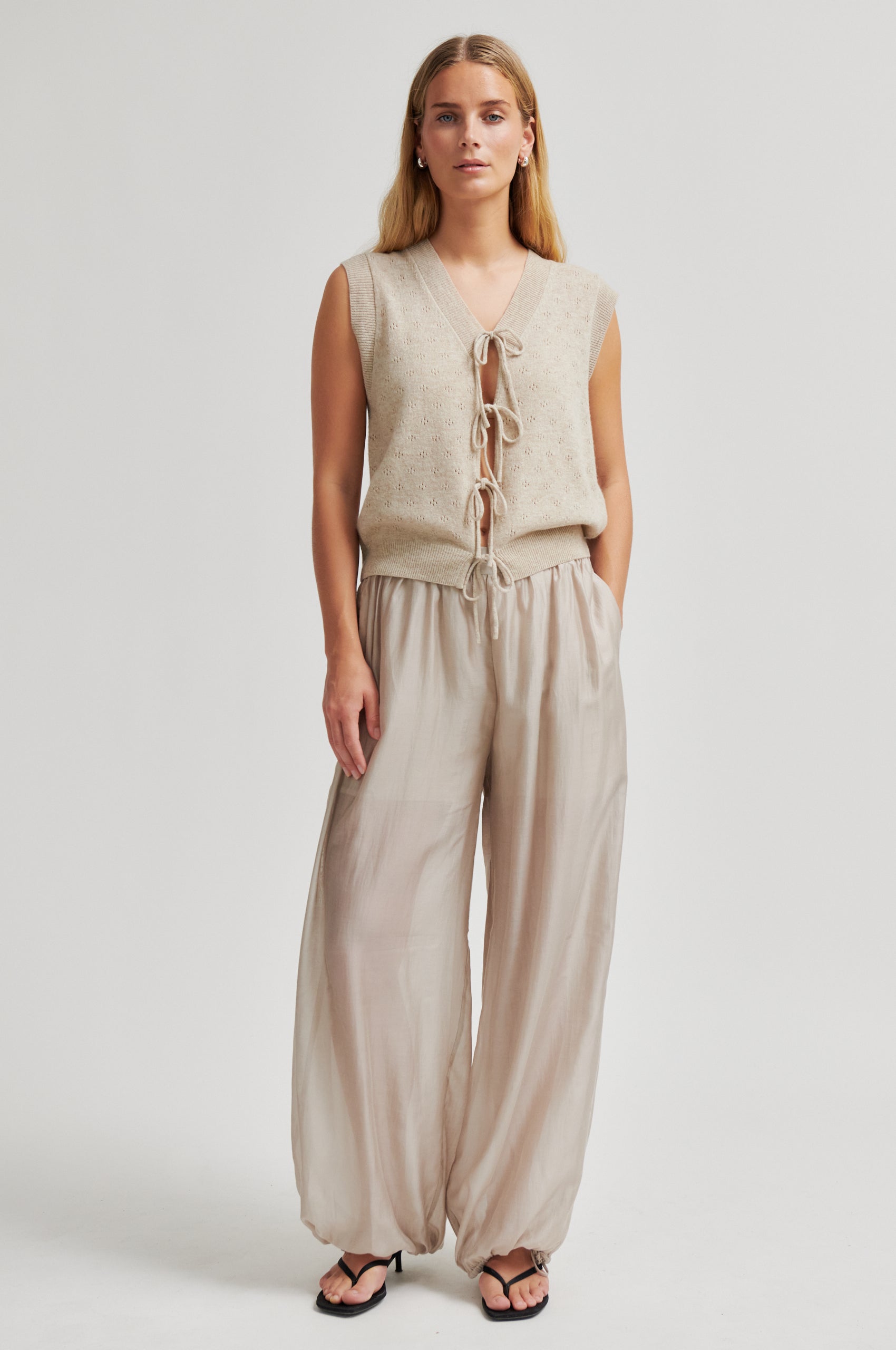 Woman wearing a beige sleeveless top and wide-leg pants on a white background from second Female
