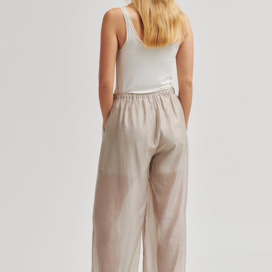 Woman wearing beige wide-leg pants and a white top on a light gray background