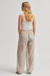 Woman wearing beige wide-leg pants and a white top on a light gray background