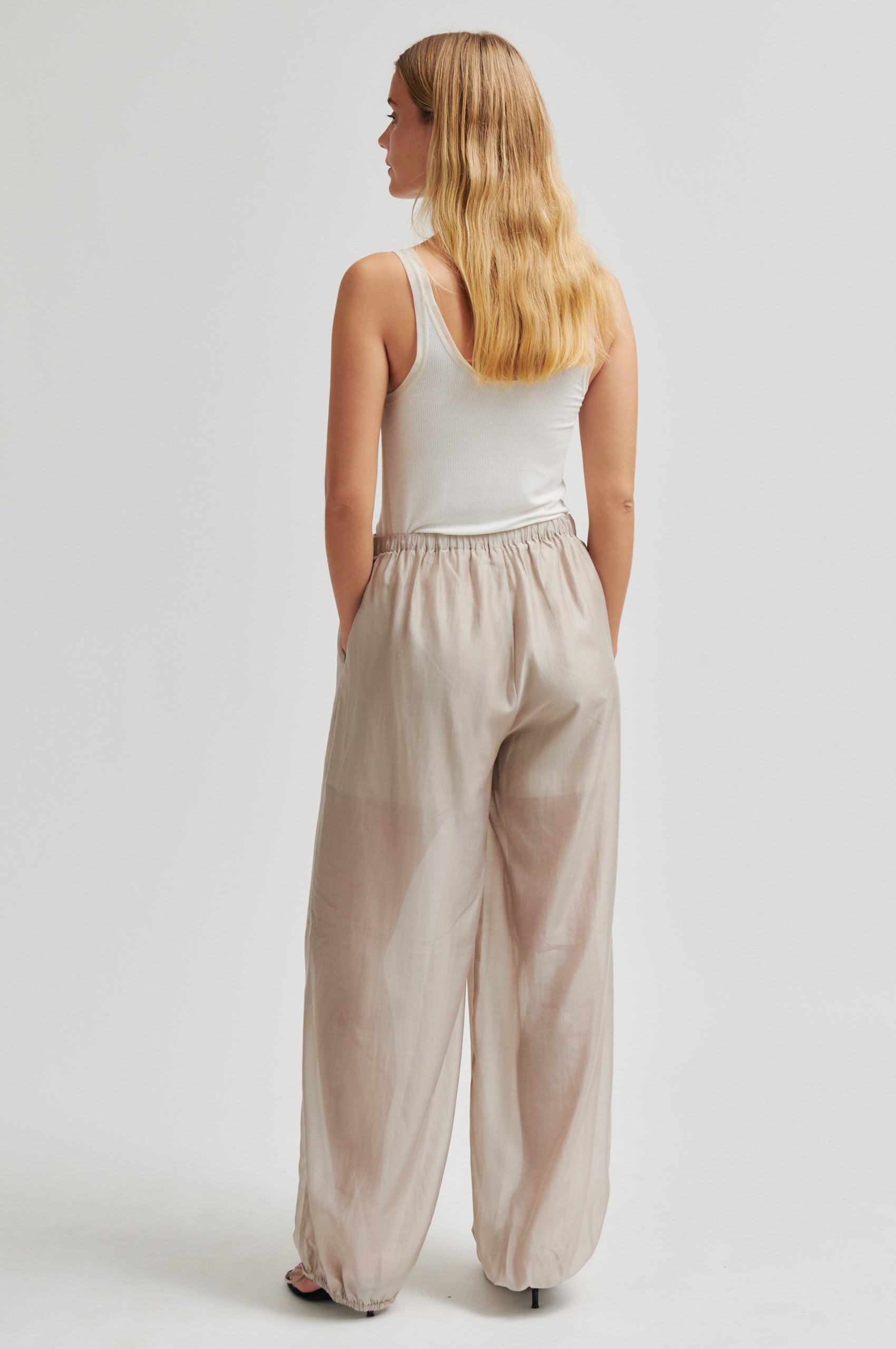 Woman wearing beige wide-leg pants and a white top on a light gray background