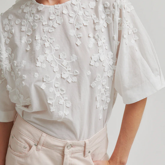White blouse with floral embroidery worn by a person on a plain background