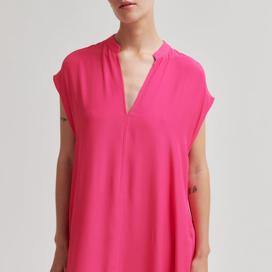 Woman wearing a bright pink dress against a plain background from Second Female