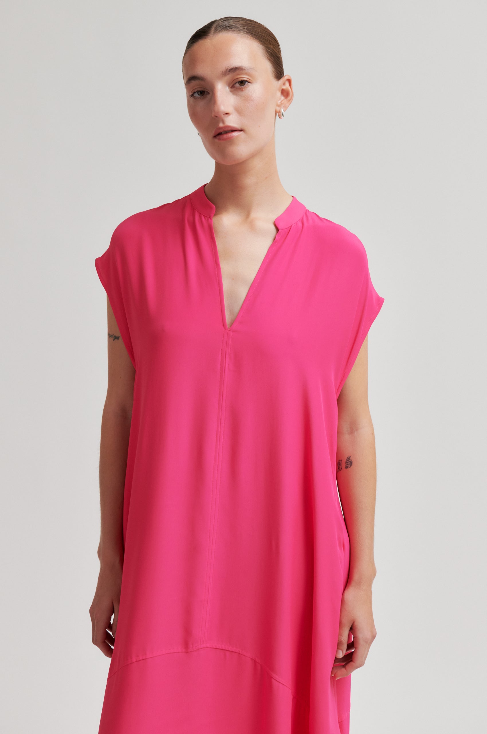 Woman wearing a bright pink dress against a plain background from Second Female