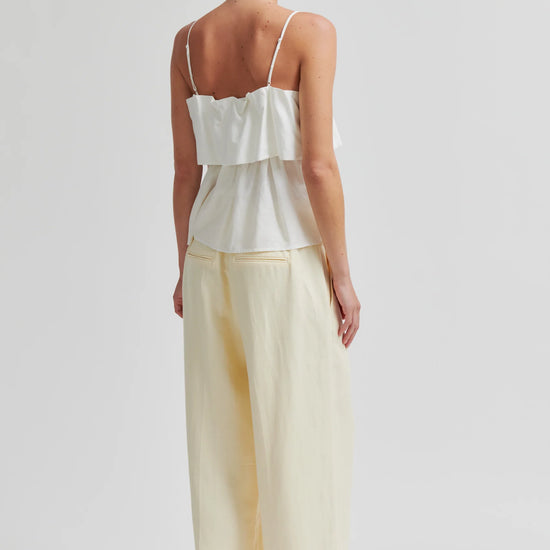 Woman wearing a white top and light yellow pants on a plain background from Second Female