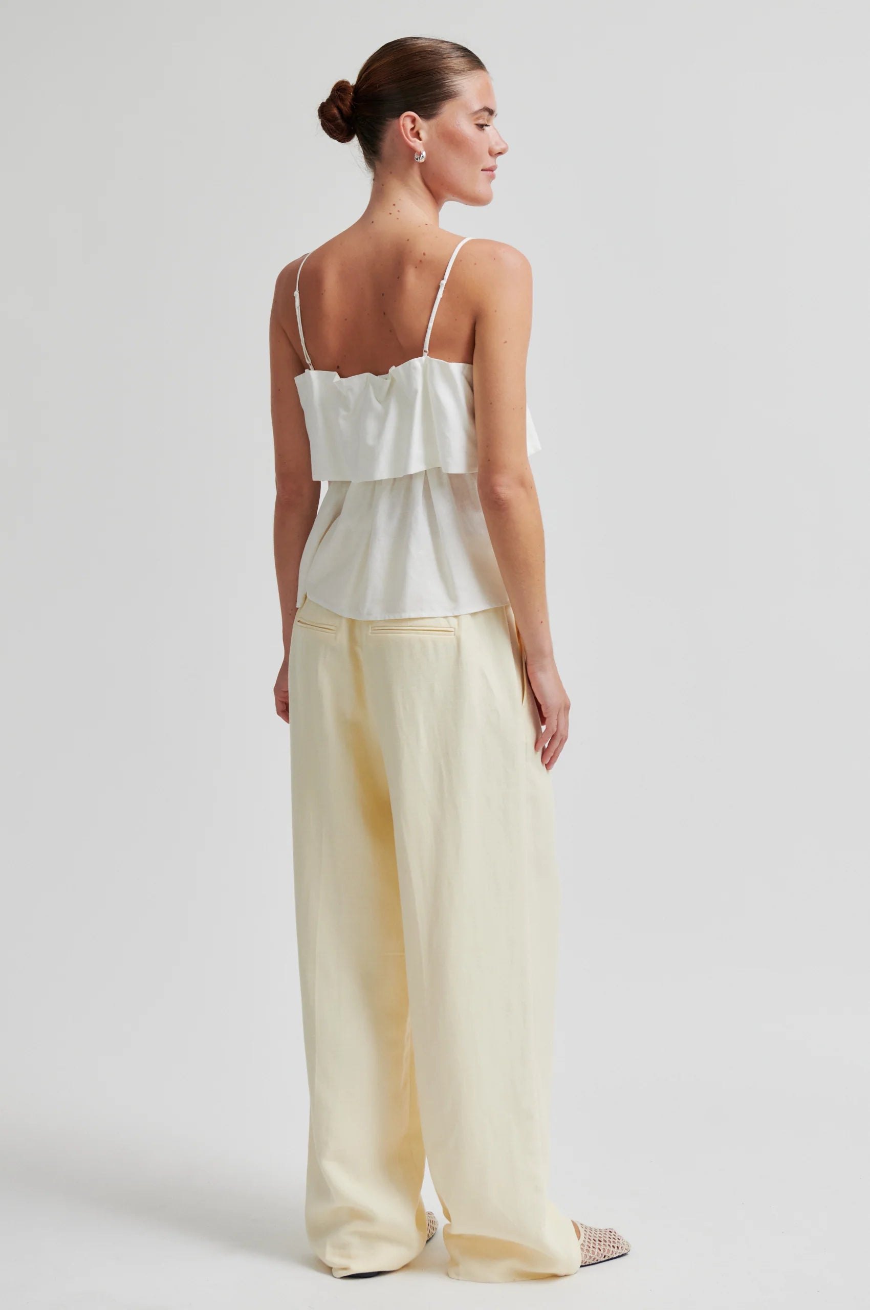 Woman wearing a white top and light yellow pants on a plain background from Second Female