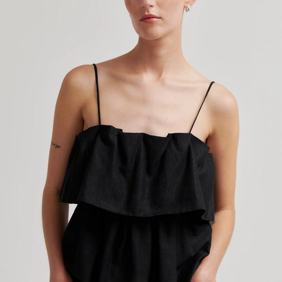 Woman wearing a black top with thin straps against a plain background from second female