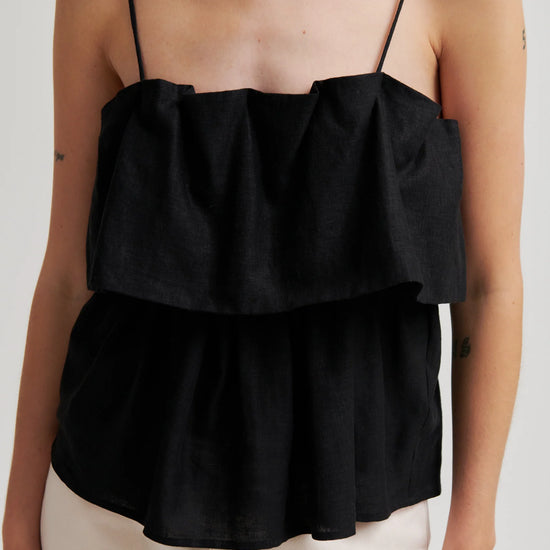 Black ruffled top worn by a person on a plain background from second female