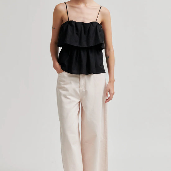 Woman wearing a black ruffled top and beige pants on a white background