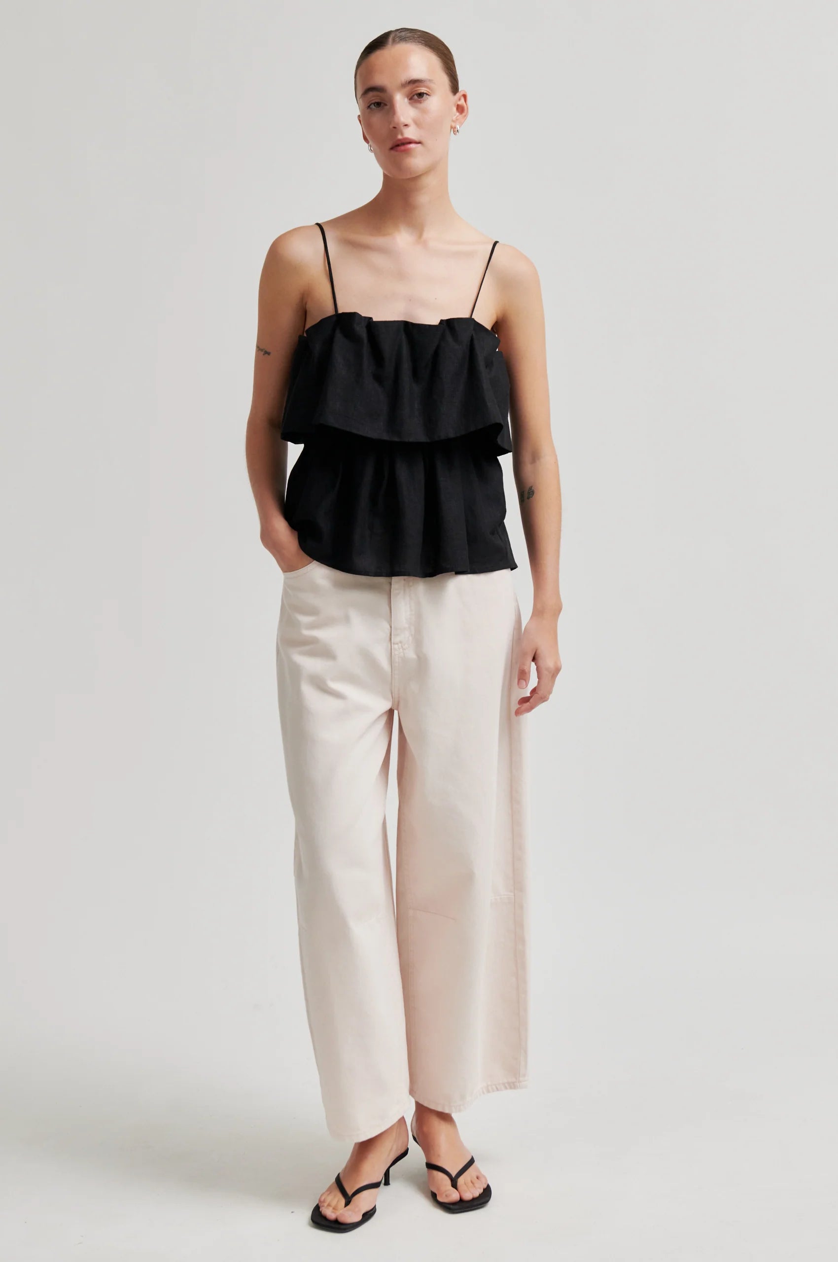 Woman wearing a black ruffled top and beige pants on a white background