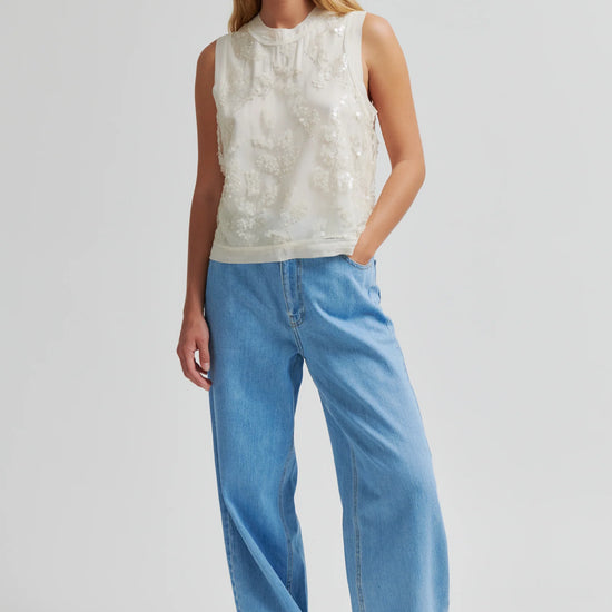 Woman wearing a sleeveless white top and blue jeans on a plain background from Second Female