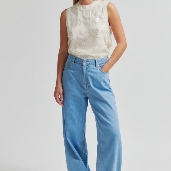 Woman wearing a sleeveless top and blue jeans on a plain background from Second Female