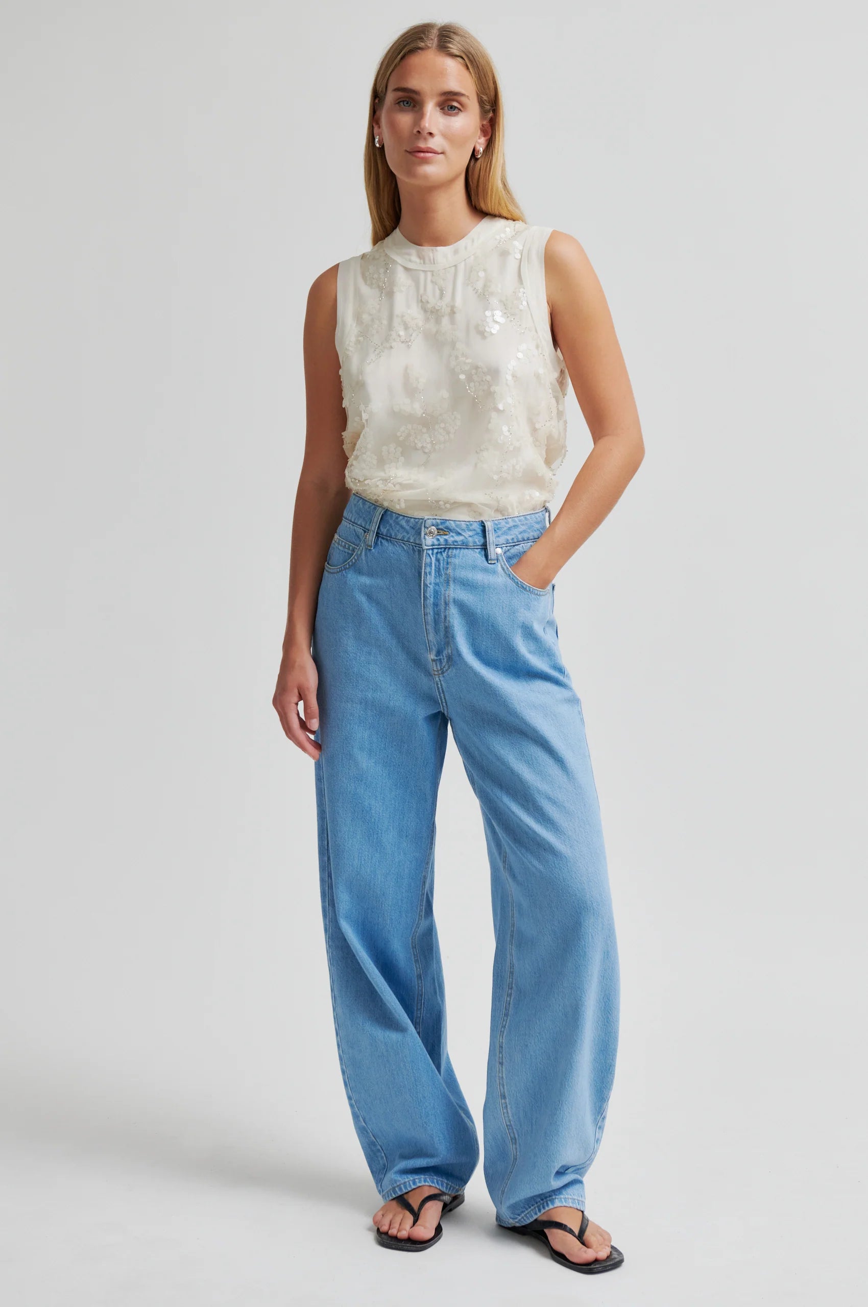 Woman wearing a sleeveless top and blue jeans on a plain background from Second Female