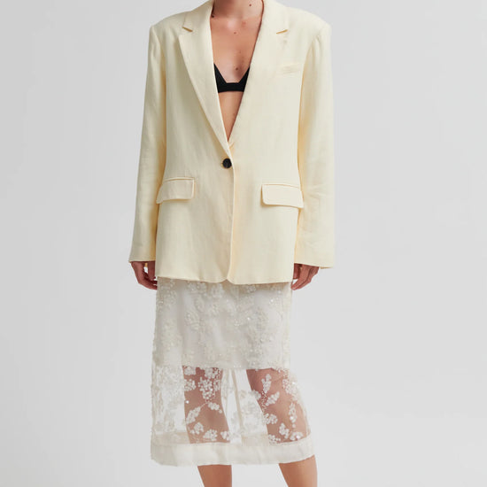 Woman wearing a light-colored blazer and lace skirt on a plain from background from Second Female 