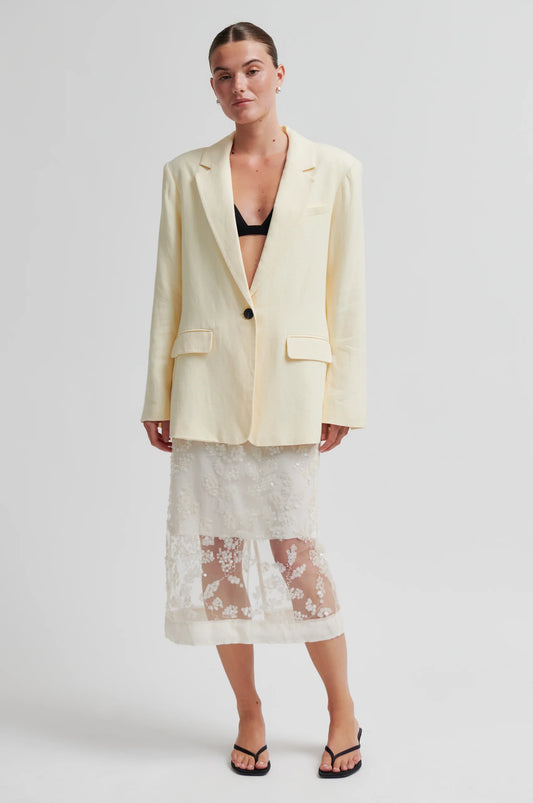 Woman wearing a light-colored blazer and lace skirt on a plain from background from Second Female 