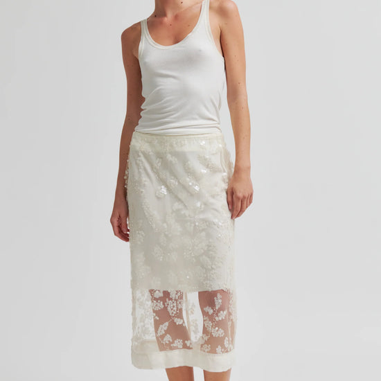 Woman wearing a white tank top and lace skirt on a plain background
