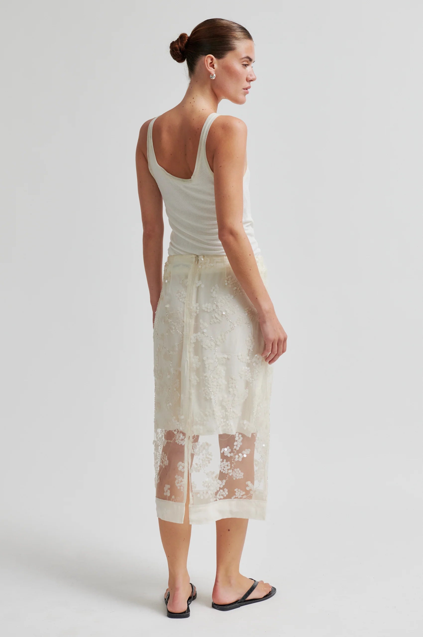 Woman wearing a white lace skirt and white tank top on a plain background from Second Female