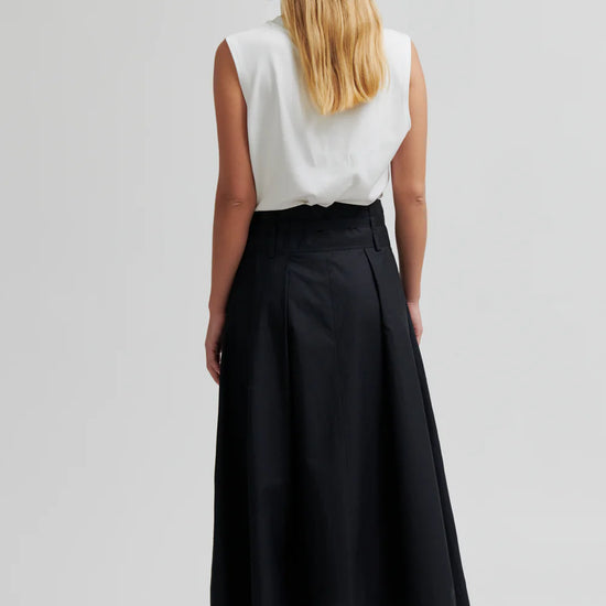 model wearing black skirt and white top facing away from camera